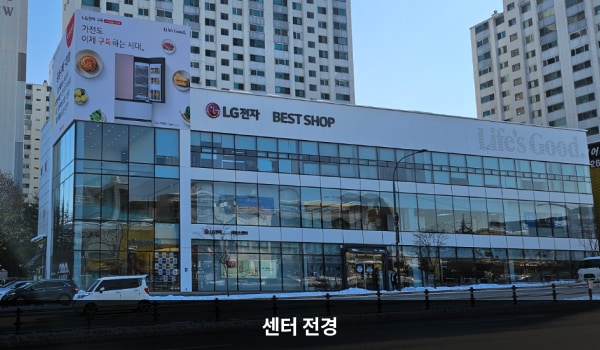 죽전서비스센터의 흰색 건물에 유리창이 크고 많습니다. 건물 3층 간판에는 'LG전자 BEST SHOP', 1층 간판에는 'LG전자 서비스센터'라고 쓰여 있습니다. 좌측으로 주차장 입구가 있습니다.