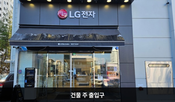 죽전서비스센터의 건물 주 출입구 위에는 'LG전자' 문구가 적혀 있습니다. 자동문으로 된 출입문 앞에 점자블록이 있으며, 왼쪽에 주차 요금 정산기가 있습니다. 문을 열고 들어가면 안쪽에 버튼식 자동문이 하나 더 있습니다.