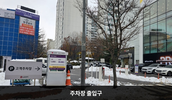죽전서비스센터의 건물 좌측, 주 출입구 앞쪽에 지상 주차장이 있습니다. 입구에 차단기가 설치되어 있으며, 왼쪽에 주차 안내 부스가 있습니다.