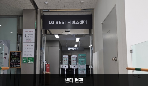 죽전서비스센터의 센터 현관 위쪽에 'LG BEST 서비스센터'라는 문구가 적혀 있으며, 그 아래에 자동문이 있습니다. 문을 열고 들어가면 앞쪽에 셀프 접수기, 좌측에 부품 판매 창구가 있습니다.
