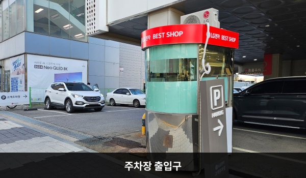 파주서비스센터의 건물 좌측에 지상 주차장이 있습니다. 주차장 입구 오른쪽에는 'LG전자 BEST SHOP' 문구가 적힌 주차 안내 부스가 있습니다.