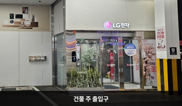 서안산서비스센터의 1층 주차장을 통해 들어갈 수 있는 자동문 출입구가 있으며, 문 앞에 점자블록이 있습니다. 문 위에 'LG전자'라고 쓰여 있습니다. 출입문을 열고 들어간 후에 문이 한 번 더 있고, 왼쪽에 엘리베이터와 계단이 있습니다.