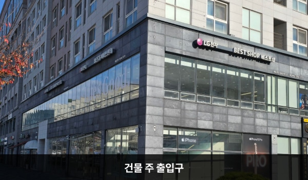 세종서비스센터의 건물 정면 'LG전자 BEST SHOP 베스트샵' 간판 왼쪽 아래에 회색 돌벽으로 둘러싸인 주 출입구가 있습니다. 유리문으로 되어 있으며, 양쪽 문 안쪽에 긴 손잡이가 있고 입구 우측으로 엘리베이터가 있습니다.