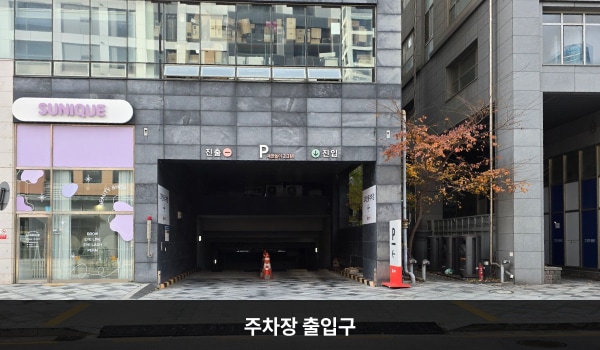 세종서비스센터의 건물 뒤쪽에 지하 주차장 출입구가 있습니다. 출입구 오른쪽에 'P'라는 글자가 적힌 보라색 입간판이 있으며, 차량 제한 높이는 2.3m입니다.