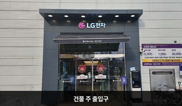 오산서비스센터의 건물 주 출입구 위에 'LG전자'라는 문구가 적혀 있고, 문 앞쪽에 점자블록이 있습니다. 출입문은 자동문이며, 오른쪽 문 안쪽에 문 열림 버튼이 있습니다. 문을 열고 들어오시면 자동문이 하나 더 있습니다.