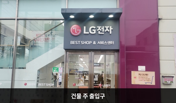 동광주서비스센터의 건물 우측에 주 출입구가 있습니다. 출입구 위에는 검은 바탕에 'LG전자', 'BEST SHOP & 서비스센터'라고 적혀 있습니다. 문 앞에 경사진 턱이 있으며, 양쪽 유리문 안쪽에 긴 손잡이가 있습니다.