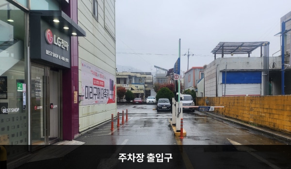 동광주서비스센터의 건물 뒤쪽에 주차장이 있으며, 주차장 출입구는 건물 오른쪽에 있습니다. 출입구 오른쪽에는 '주차장 이용 안내'라고 적힌 보라색 팻말이 붙어 있습니다.