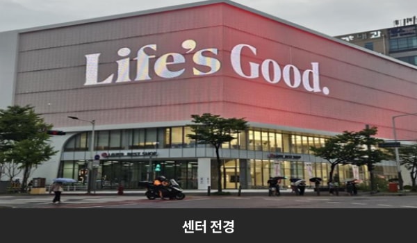 둔산서비스센터의 흰색 건물 맨 위층을 둘러싼 붉은 간판에 'Life's Good', 'LG전자 서비스센터, BEST SHOP'이라고 쓰여 있습니다. 건물의 1층과 2층은 유리창으로 되어 있습니다.