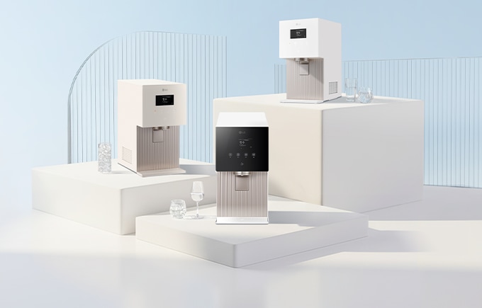 깨끗하고 밝은 톤의 공간 속 서로 다른 높이의 단상 위에 세 대의 LG 퓨리케어 정수기가 놓여 있으며, 주변에는 투명한 유리컵과 물방울 오브제가 배치되어 있는 이미지입니다.