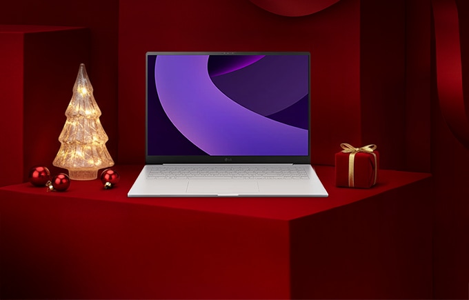 레드 기프트 박스 배경 위에 LG 그램 노트북이 놓여 있고, 좌측에는 조명 트리, 우측에는 리본이 묶인 선물이 배치된 연말 분위기의 구성.