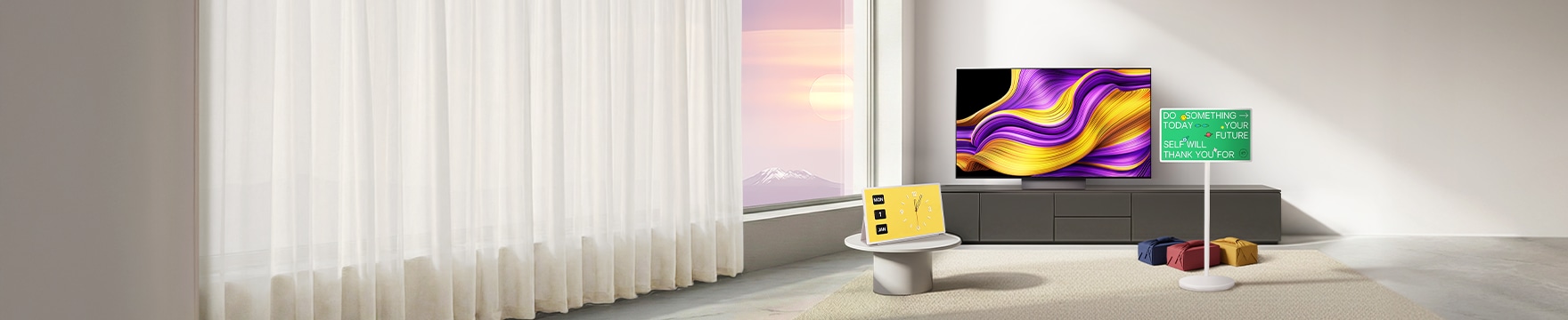 자연광이 드는 미니멀한 거실에 추상 그래픽 화면의 올레드 TV가 정면에 보이고 노란 디지털 시계 화면에 스탠바이미가 놓인 테이블, 초록색 문구 화면 스탠바이미와 선물이 배치된 장면.