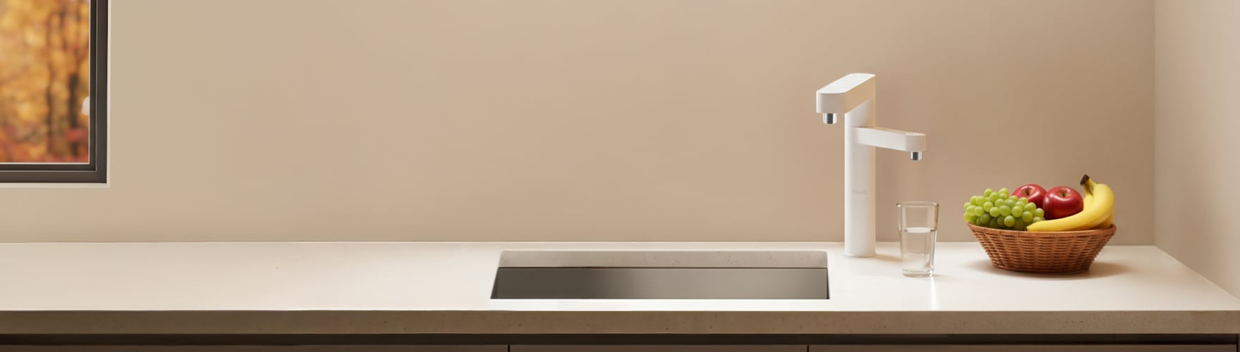 주방 싱크대 위에 LG 퓨리케어 정수기가 놓여 있고, 옆에는 유리컵과 과일 바구니가 함께 배치된 깔끔한 인테리어 공간.