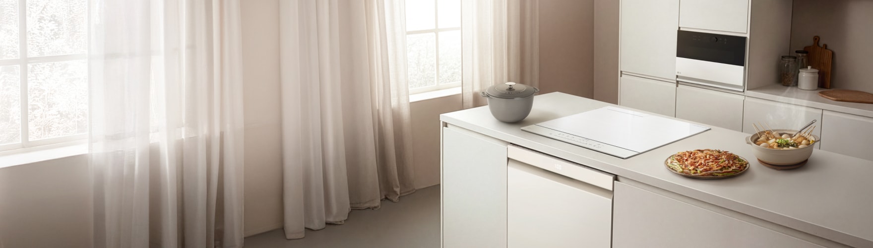 밝은 톤의 주방 공간에 흰색 아일랜드 식탁과 LG전자 식기세척기, 인덕션, 광파오븐이 설치되어 있으며, 식탁 위에는 피자와 샐러드 등의 음식이 놓여 있고, 창가에는 흰색 커튼이 드리워져 있다.