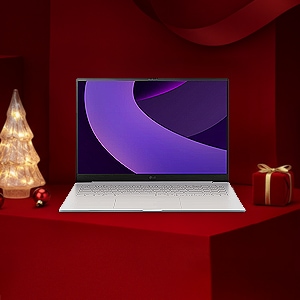 레드 기프트 박스 배경 위에 LG 그램 노트북이 놓여 있고, 좌측에는 조명 트리, 우측에는 리본이 묶인 선물이 배치된 연말 분위기의 구성.