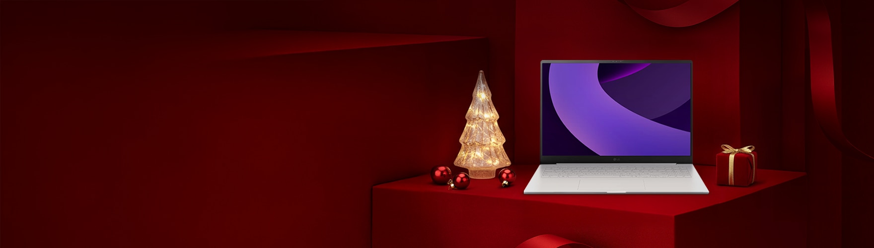 레드 기프트 박스 배경 위에 LG 그램 노트북이 놓여 있고, 좌측에는 조명 트리, 우측에는 리본이 묶인 선물이 배치된 연말 분위기의 구성.