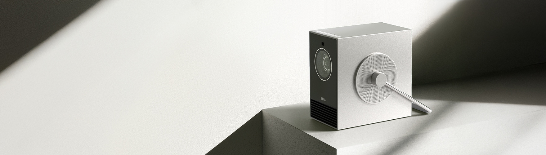 미니멀한 실내 공간에 놓인 프로젝터 ‘시네빔 큐브’. 은은한 실버 컬러의 본체 전면에는 렌즈가 보이고, 부드러운 자연광이 제품을 비추고 있다.