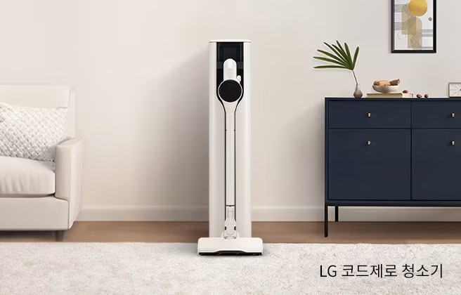 거실공간에 무선청소기가 놓여있습니다. 소파, 러그, 수납장 등이 보입니다.