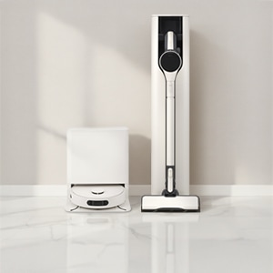 밝은 빛이 비추는 흰색 톤 실내 공간에 로봇 청소기와 무선청소기가 나란히 놓여있습니다.