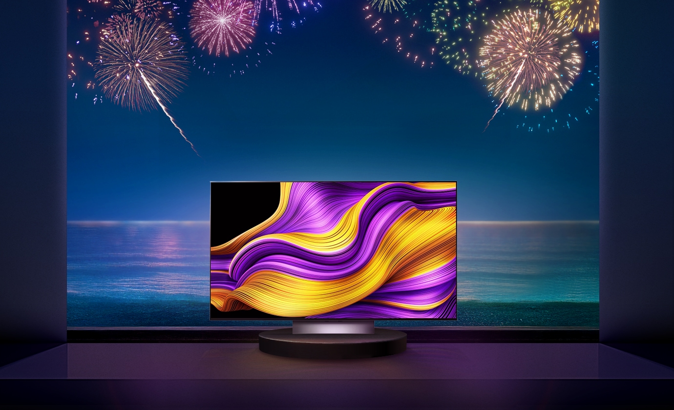 불꽃이 터지는 바다 배경 앞에 LG 올레드 스탠드형 TV가 중앙에 놓여져 있습니다.