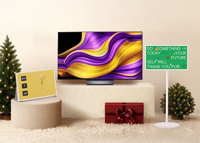 따뜻한 실내 공간에 두 그루의 작은 크리스마스 트리 사이로 올레드 TV, 스탠바이미가 놓여 있는 모습.