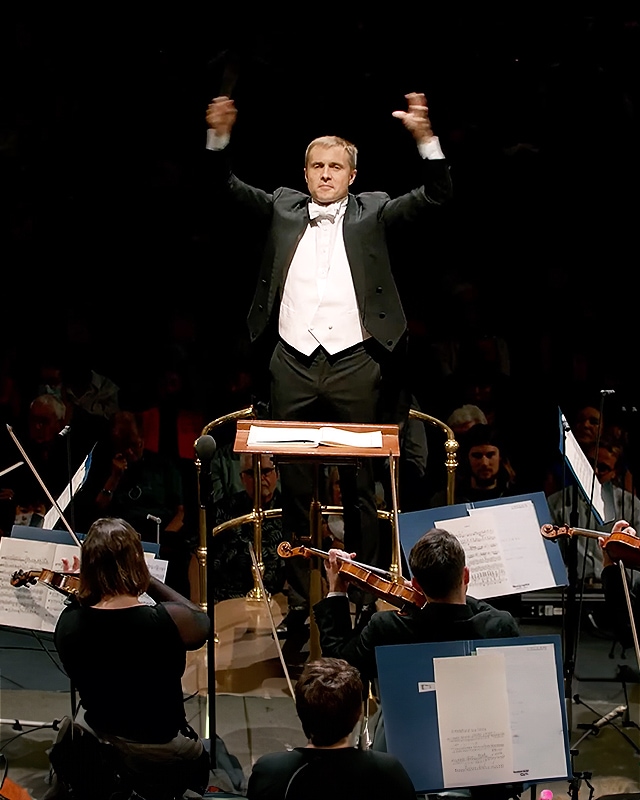 한 손을 들고 오케스트라를 지휘하는 지휘자.