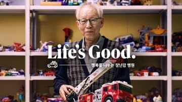 장난감 병원에서 소방차 장난감을 들고 있는 노년의 남성. Life is Good이라는 글씨가 있다.
